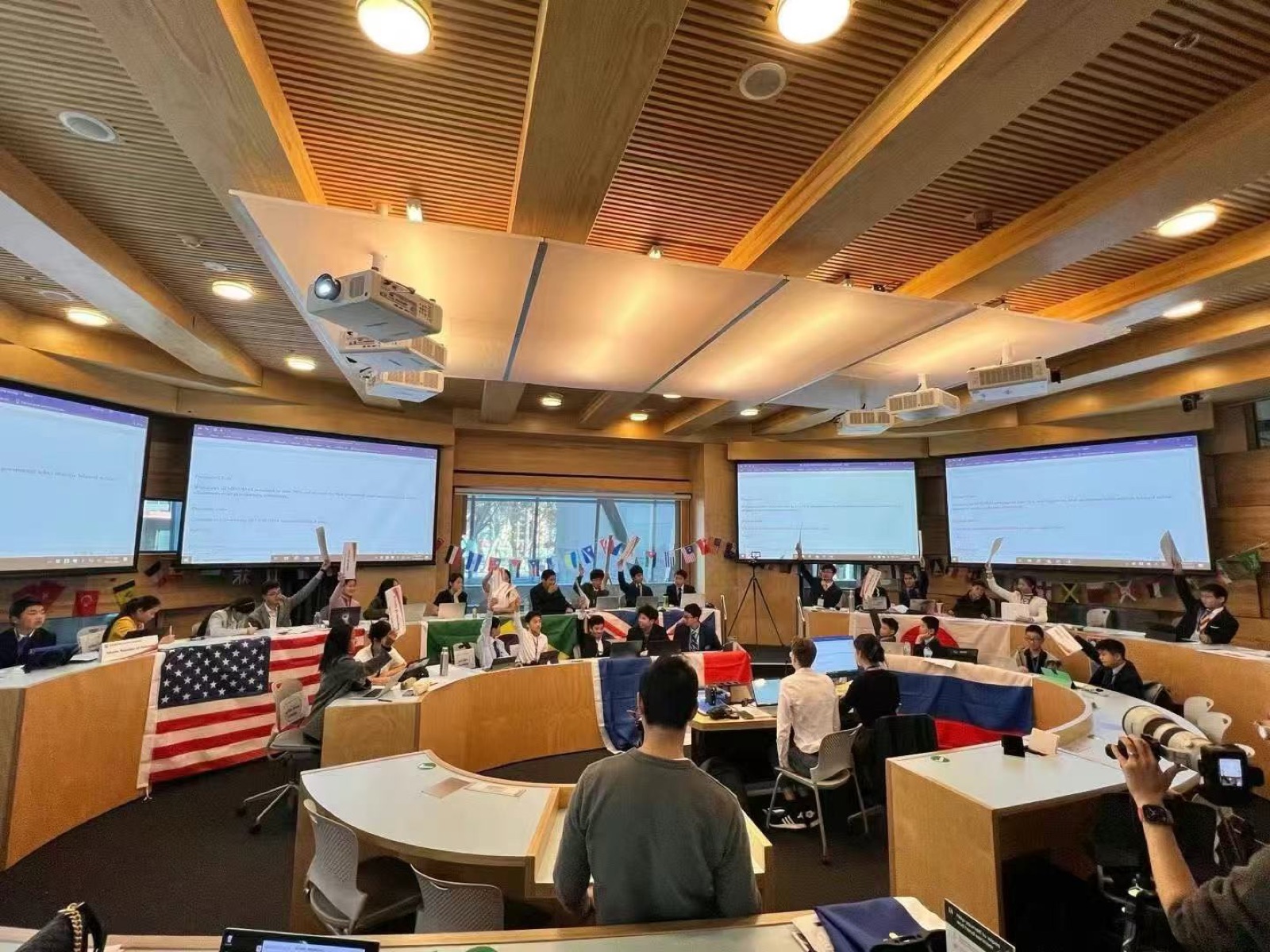 学生们手持各国国旗在阶梯式会场参加模拟联合国活动