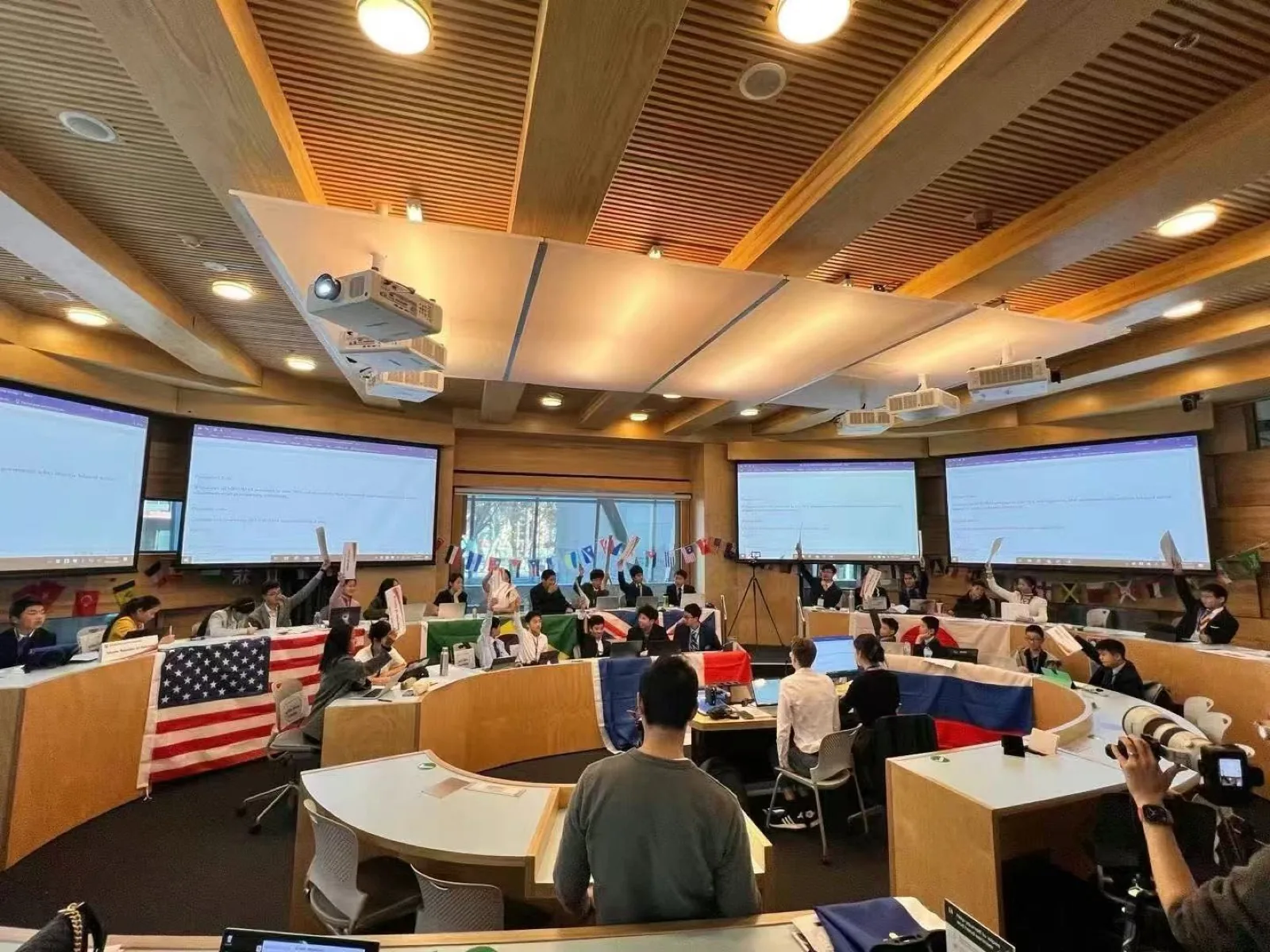 Students with country flags at a Model UN event in a tiered hall